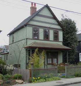 maison grise à pignon sur deux étages avec garniture bordeaux et véranda