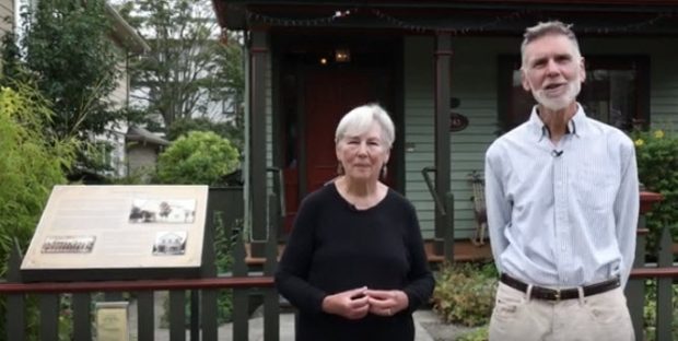 couple âgé sur le trottoir devant la maison. La femme a les mains croisées et l’homme a les mains derrière le dos