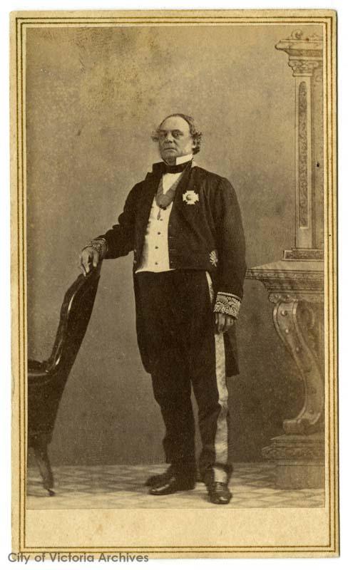 portrait professionnel officiel d’un homme âgé debout, vêtu d’un smoking avec col ailé et médaille au revers