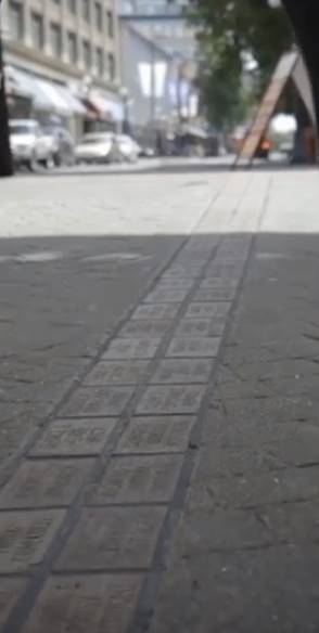 Square public montrant une double rangée de briques grises insérées dans le pavé où des noms y sont gravés