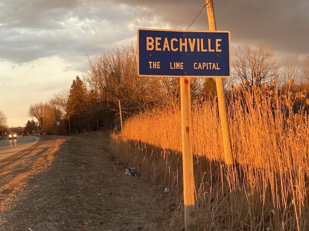 Une photographie couleur d'un panneau routier bleu à côté des hautes herbes, le panneau indique Beachville The Lime Capital