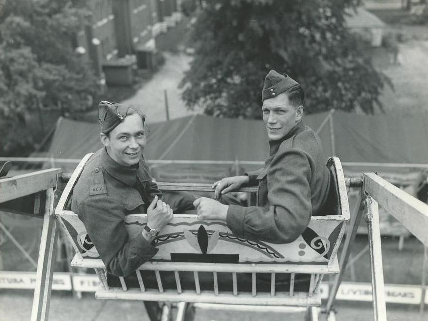 Une photo en noir et blanc de deux soldats en uniforme, assis dans la grande roue, on peut voir les lettres RCA sur l’épaulette d’un des soldats