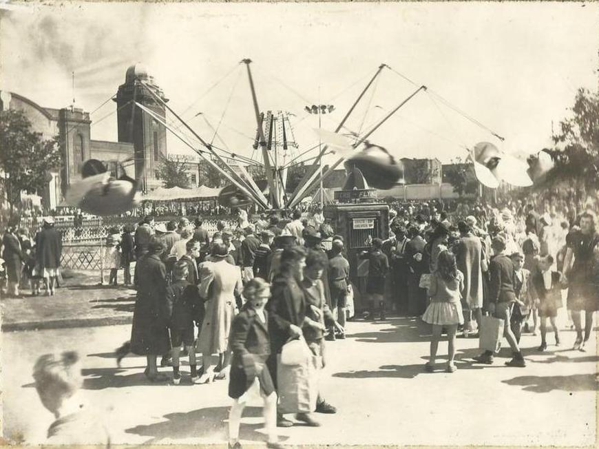 Une photo en noir et blanc d’un grand manège à rotation de la fête foraine; on voit aussi partiellement le manège Flying Scooters