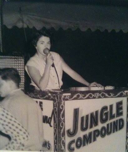 Une photo en noir et blanc d’une femme tenant un microphone derrière un podium sur lequel il est écrit « Jungle Compound », ce qui veut dire enceinte de la jungle