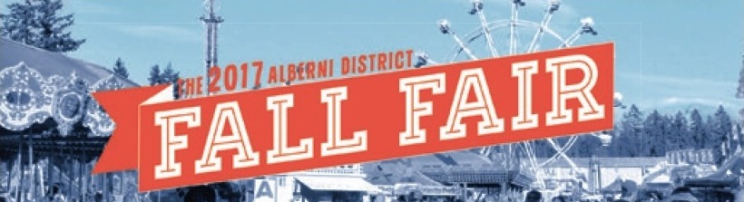 Un panneau publicitaire du Port Alberni District Fall Fair 2017 (foire automnale du District de Port Alberni 2017); en arrière-plan, on voit la fête foraine