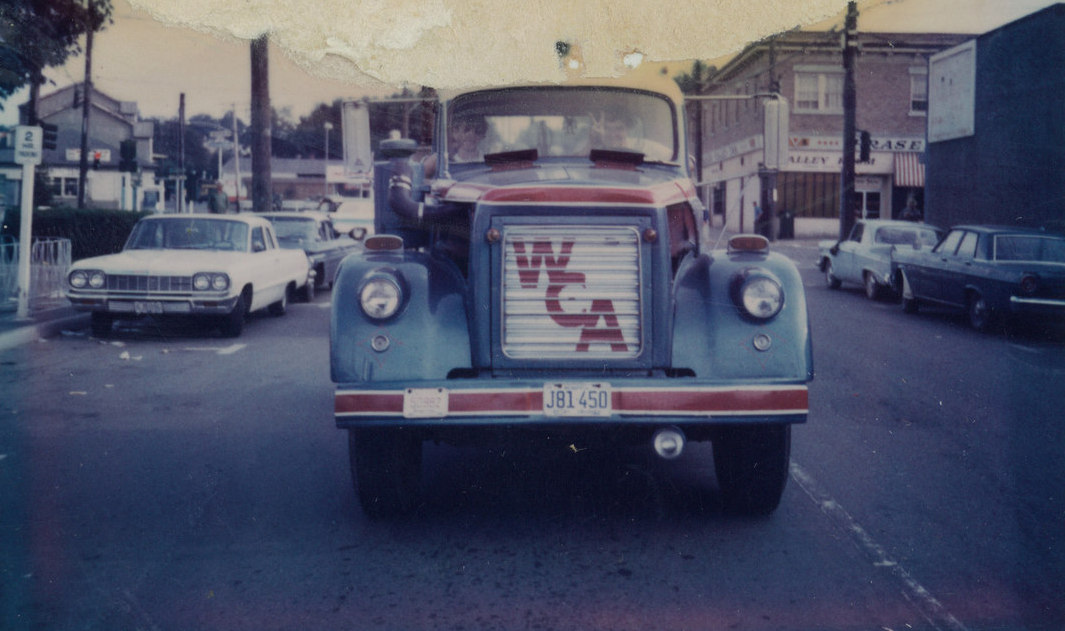 Un camion d’époque qui roule dans une rue, et sur lequel figurent les lettres WCA sur le devant