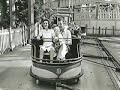 Vignette d’une photo en noir et blanc de gens dans un manège forain constitué d’une voiturette ouverte sur des rails