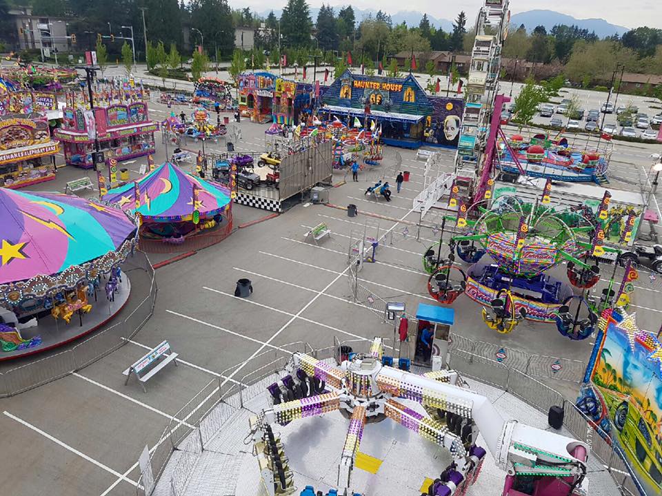 Une vue d’ensemble des attractions d’une fête foraine montées dans un stationnement, il y a beaucoup de manèges et de stands