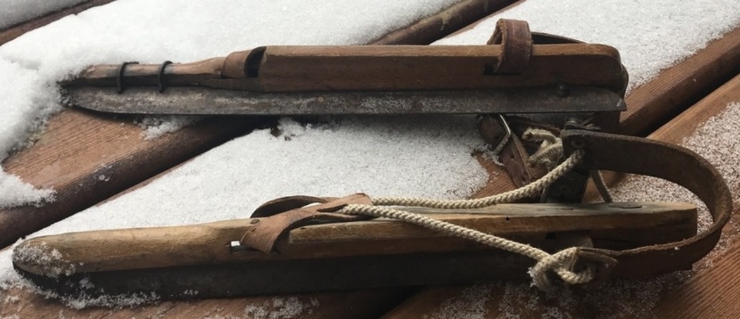 Gros plan d’une vieille paire de patins de vitesse; il n’y a pas de chaussures, seulement des cordes et une sangle en cuir attachés à un morceau de bois sous lequel est placée la lame