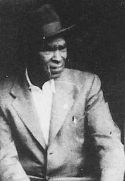 Photo d’archives en noir et blanc d’un homme noir portant un costume et un chapeau.