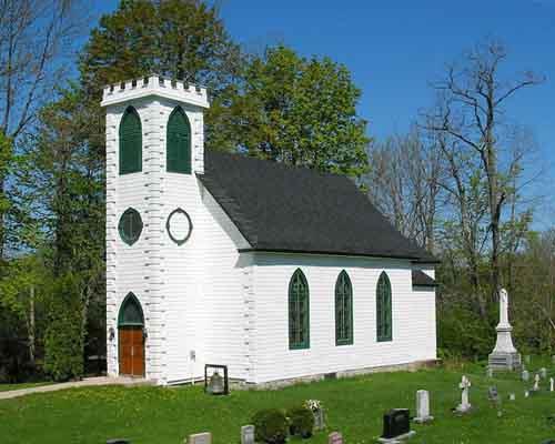 Photographie en couleurs montrant l’extérieur de l’église anglicane Saint Peter avec le cimetière à droite.