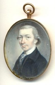 Médaillon en or avec le portrait d’un homme aux cheveux blancs portant une veste noire et un foulard blanc.