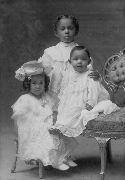 Photo en noir et blanc de deux jeunes filles noires et d’un garçon noir portant du blanc.