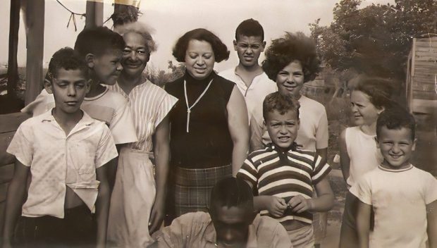 Photo d’archive en noir et blanc d’une famille de dix personnes comprenant des adultes et des enfants se tenant devant un porche.