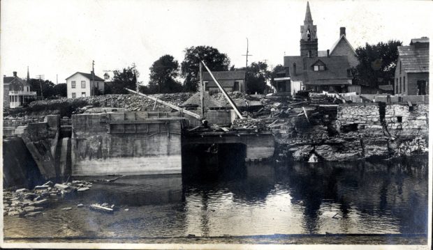 Travaux de construction sur une rivière, avec une église à l’arrière-plan. 