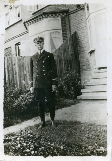 Un homme en uniforme d’aviateur, debout devant une clôture en bois.