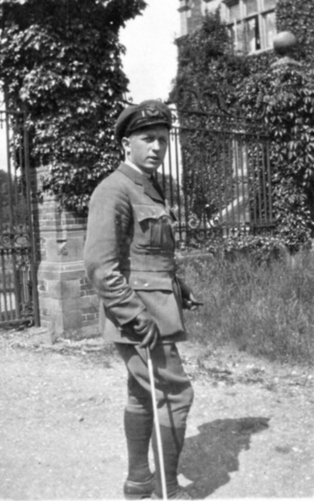 Un homme en uniforme militaire pose, l’air détendu, devant une grille en fer forgé. 