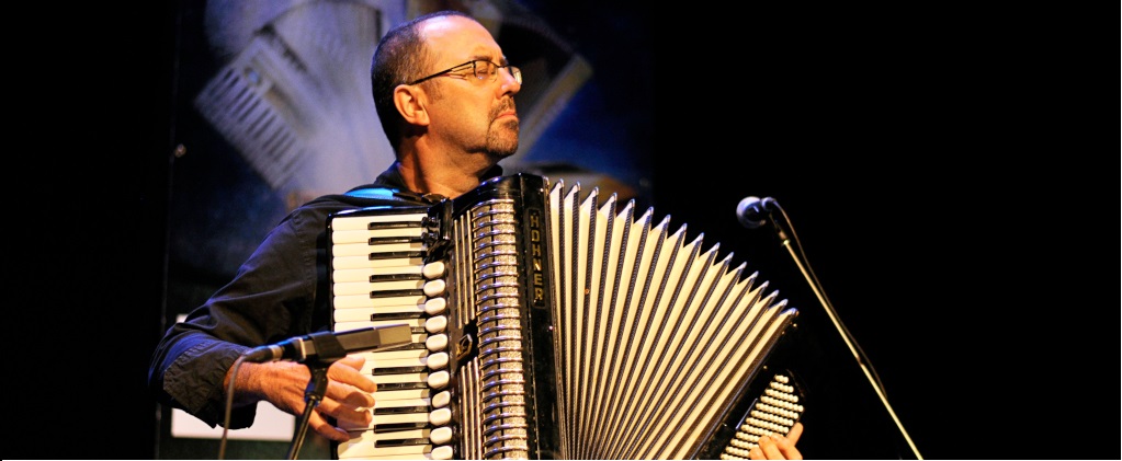 Photographie couleur où Martin Bellemare debout avec un accordéon-piano, les yeux fermés, joue face au public