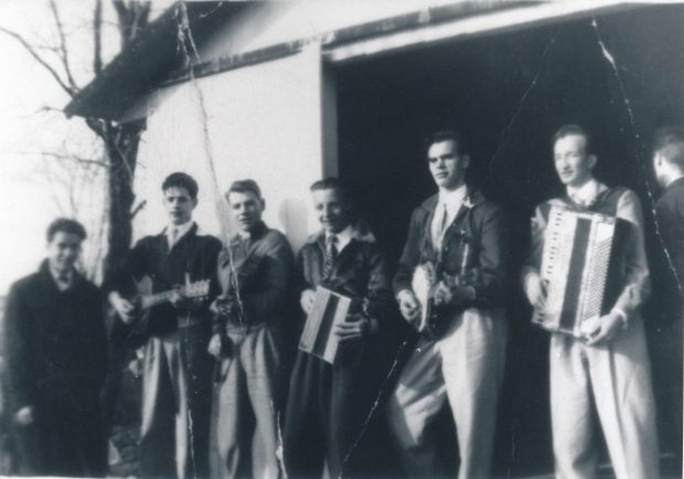 Photographie noir et blanc où sept hommes, composant un orchestre, pose devant une cabane à sucre.