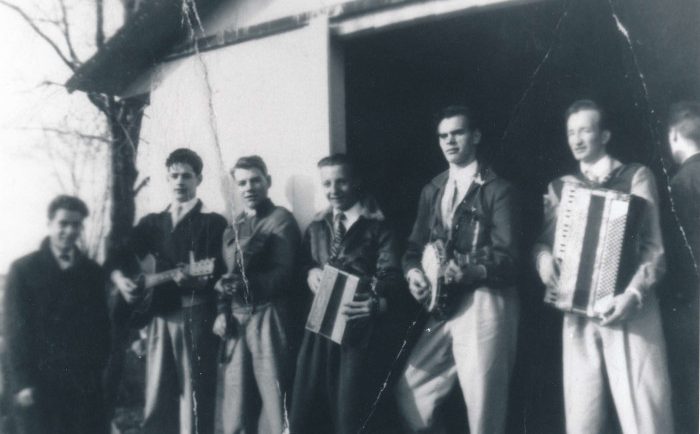 Photographie noir et blanc où sept hommes, composant un orchestre, pose devant une cabane à sucre.