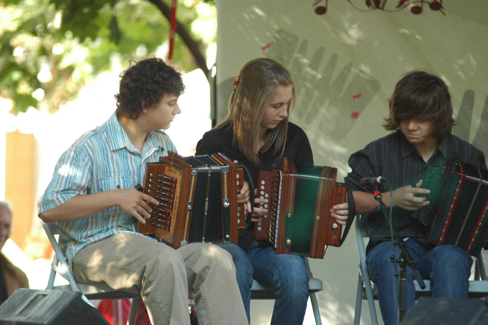 Photographie couleur, trois jeunes accordéonistes assis et très concentrés, jouent pour la première fois devant public. 