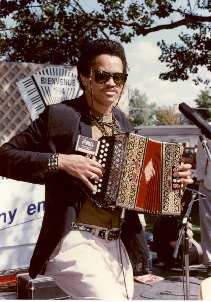 Photographie couleur, Joaquin Diaz, son accordéon diatonique en main joue à l'extérieur par une belle journée ensoleillée. 