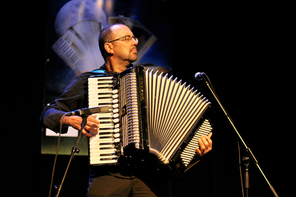 Photographie couleur où Martin Bellemare debout avec un accordéon-piano, les yeux fermés, joue face au public.