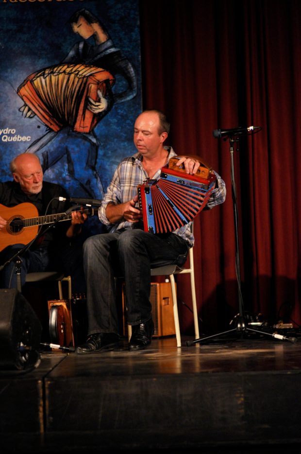 Photographie couleur où, au premier plan, Stéphane Landry joue de l'accordéon diatonique. Derrière lui, se trouve Bruno Gendron à la guitare acoustique.