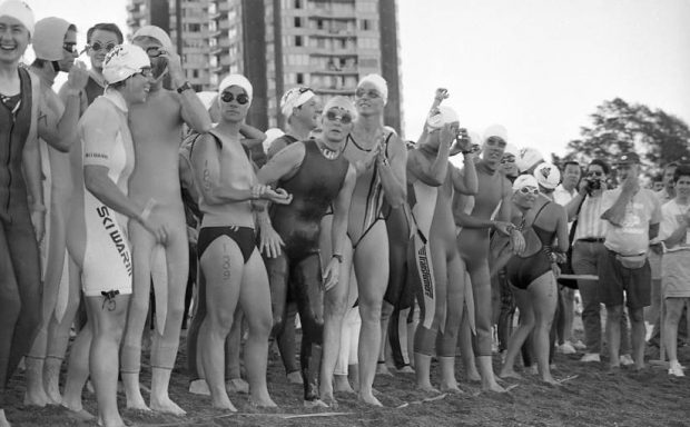  Photo en noir et blanc de femmes athlètes de triathlon en maillot de bain, lunettes et bonnets de bain, rassemblées sur la ligne de départ sur la plage à English Bay, se préparant pour la portion de natation de 1,5 km de l'événement.