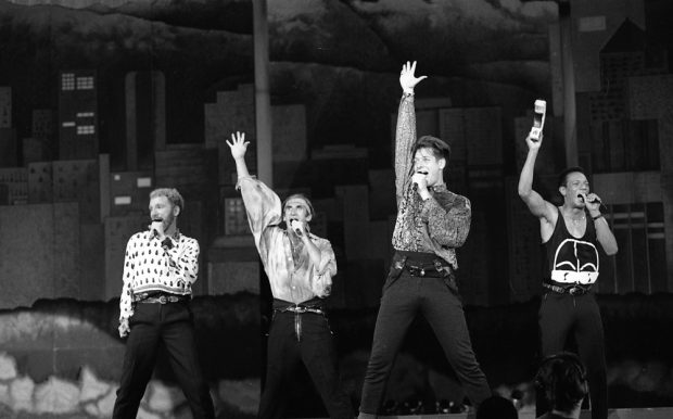  Une photo en noir et blanc des quatre membres masculins du groupe canadien a cappella, The Nylons, prenant une pose - position des jambes larges, micro dans une main et l'autre droit vers le toit - alors qu'ils se produisent sur le B.C. Place la scène du stade pour les cérémonies de clôture.
