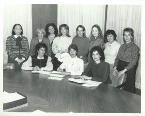 Une photographie en noir et blanc d’un groupe de femmes autour d’une table.