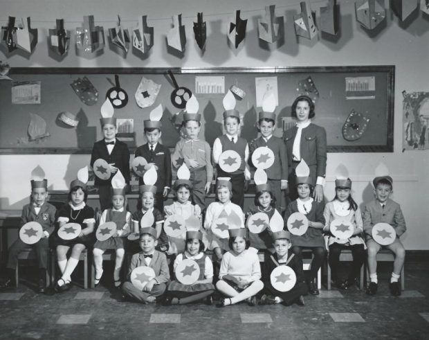 Une photographie en noir et blanc d’un groupe d’enfants dans une salle de classe qui célèbre Hanoucca.