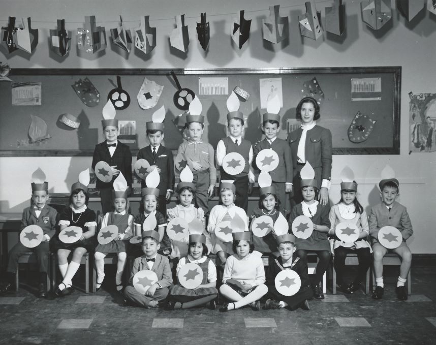 Une photographie en noir et blanc d’un groupe d’enfants dans une salle de classe qui célèbre Hanoucca.