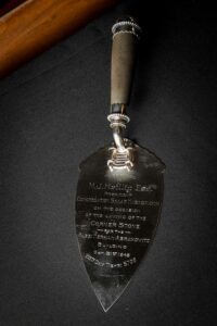 Un gros-plan d’une truelle en argent, gravée d’une inscription en anglais.