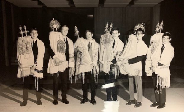 Une photographie en noir et blanc de 6 adolescents vêtus de châles de prière et transportant des rouleaux de la Torah.