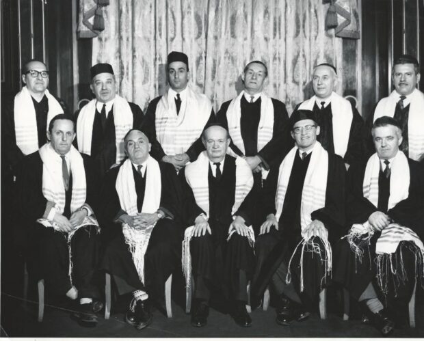 Photographie en noir et blanc d’un groupe d’hommes portant des vêtements cérémoniels et des châles de prière blancs.