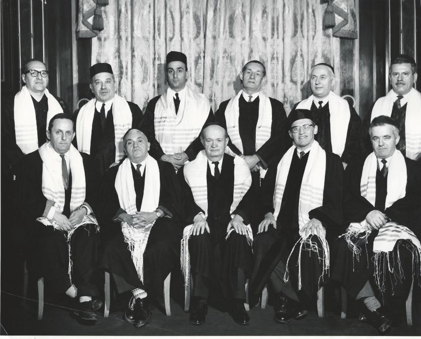 Photographie en noir et blanc d’un groupe d’hommes portant des vêtements cérémoniels et des châles de prière blancs.