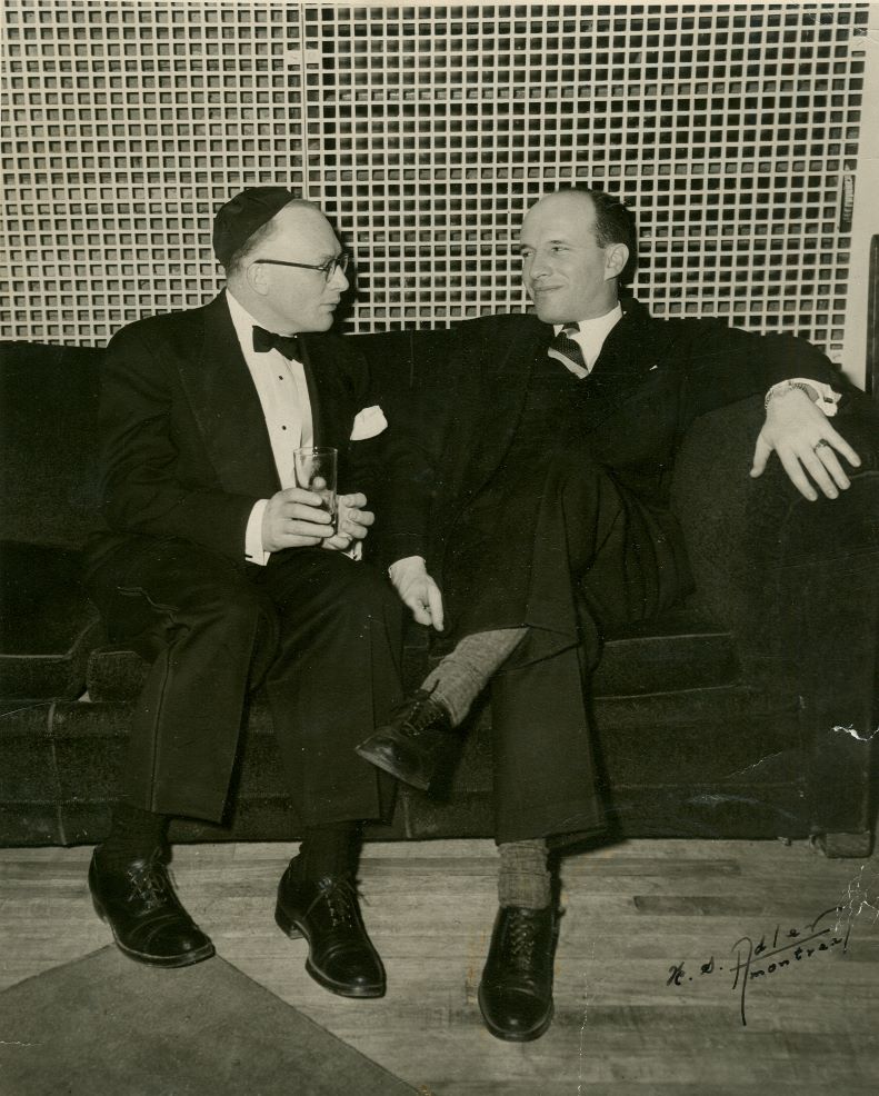 Photographie en noir et blanc de deux hommes assis sur un canapé.