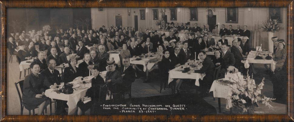 Une photographie en noir et blanc d’un groupe de personnes attablées pour un dîner.