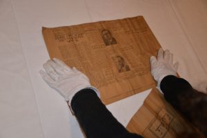 Un ancien journal yiddish déposé sur une table consulté par un individu portant des gants blancs.