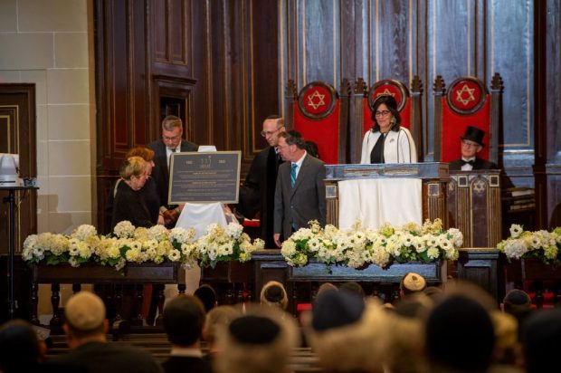 Un groupe d’individus se tient sur le podium d’une synagogue, dévoilant une plaque.