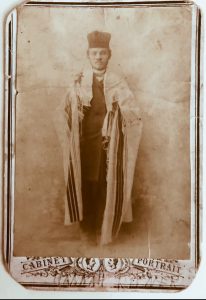 Photographie en noir et blanc d'un homme portant des robes de chantre et un châle de prière.
