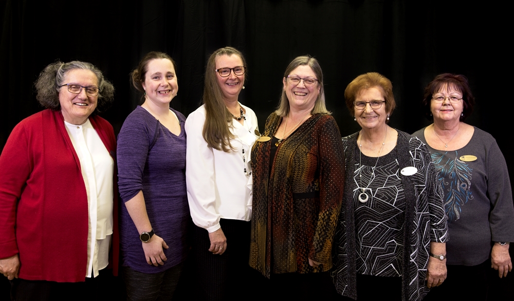 Six femmes souriantes posent l’une à côté de l’autre. 