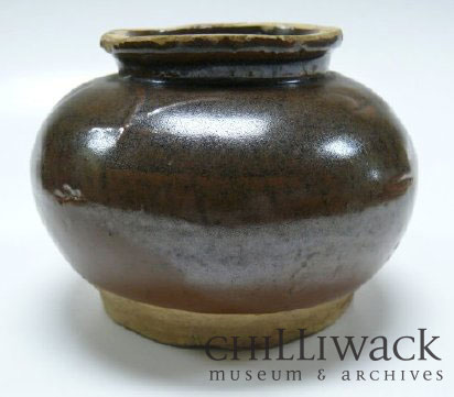 Pot en céramique rond, brun foncé verni avec une ouverture à rebord. Des personnages chinois apparaissent sur le côté du pot 