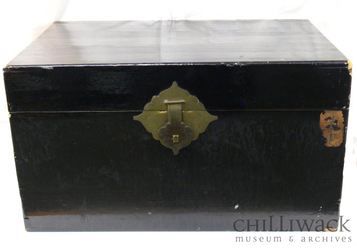 Coffre peint en noir avec quatre charnières métalliques rectangulaires et une serrure sur le devant 