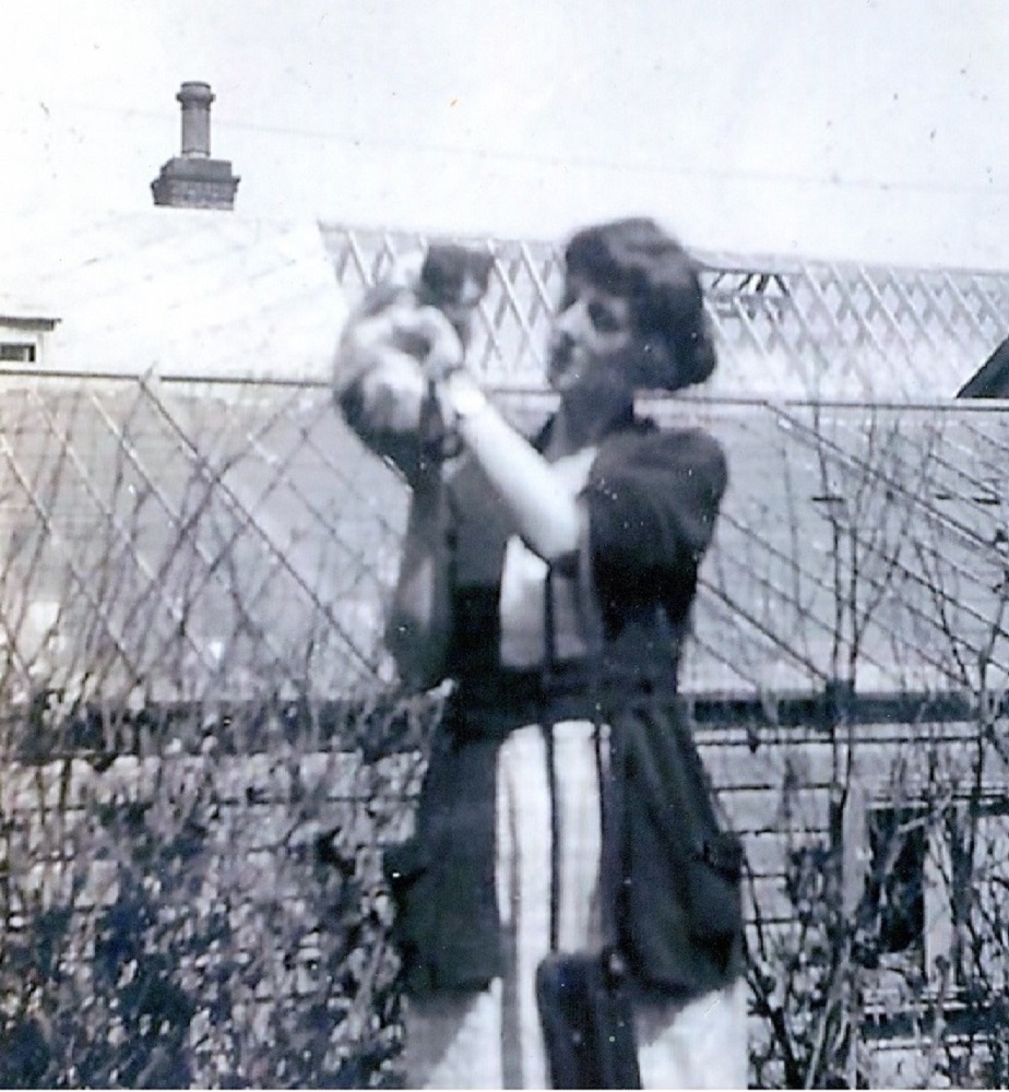 Image en noir et blanc de femmes tenant un chat, elle se tient devant deux bâtiments au toit de verre.
