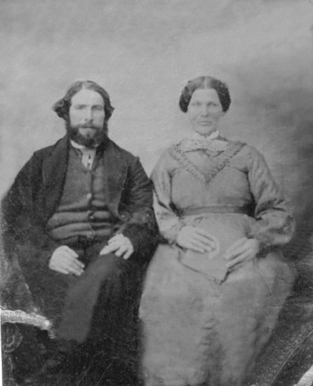 Une photo en noir et blanc d'un couple est assis, vêtue de vêtements d'époque. La femme est à droite de l'homme tout en tenant un livre.