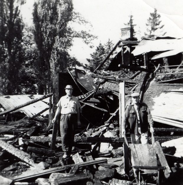 Photo noir et blanc des vestiges de la grange après l'incendie et de deux hommes du cimetière debout au milieu du rugissement.