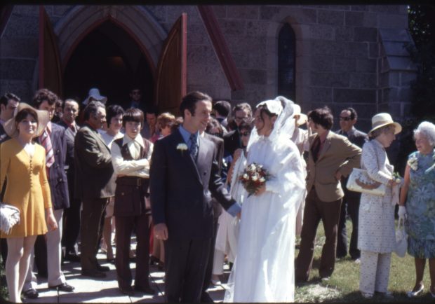 Photo couleur d'un homme et d'une femme habillés pour un mariage. Tous les deux sortant de l'église, ils sont entourés de gens.