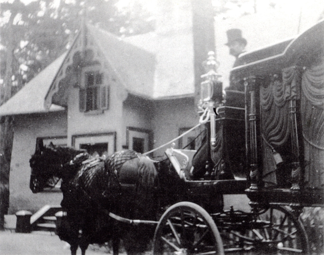 photo en noir et blanc d'un cortège funèbre, avec un corbillard à cheval entraîné et un homme portant un chapeau haut
